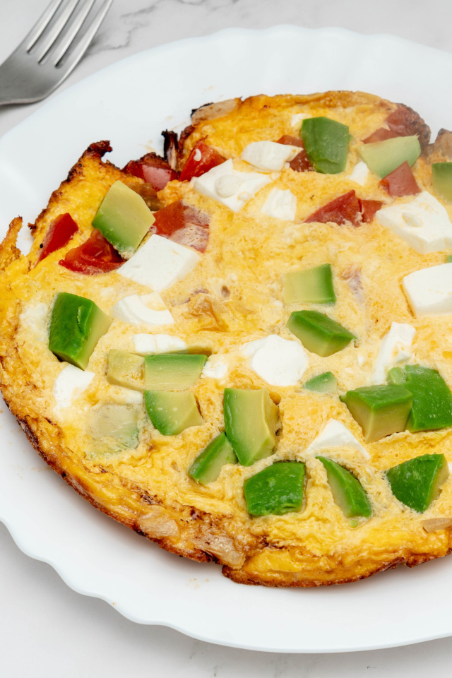 Омлет с авокадо и кусочками помидора на белой тарелке 