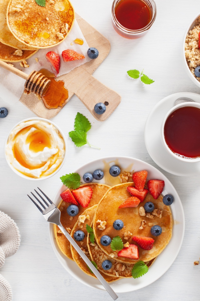 Pancakes with berries on a table with juice, tea and granola for breakfast