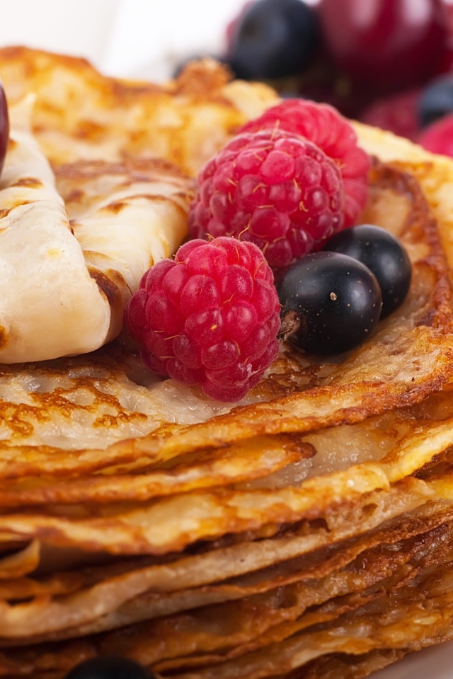 Блины с ягодами черники и малины на белой тарелке 