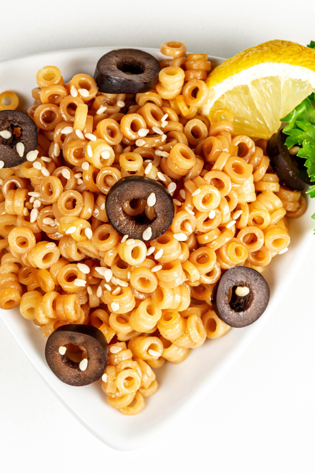 Макароны на тарелке с оливками и лимоном