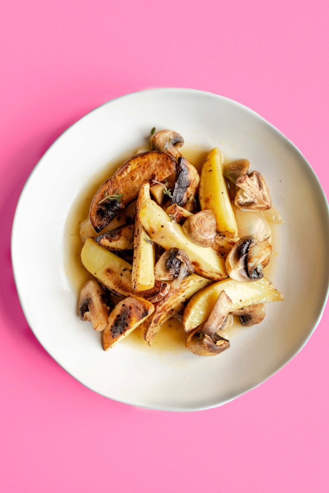 Картофель с грибами в тарелке на розовом фоне 