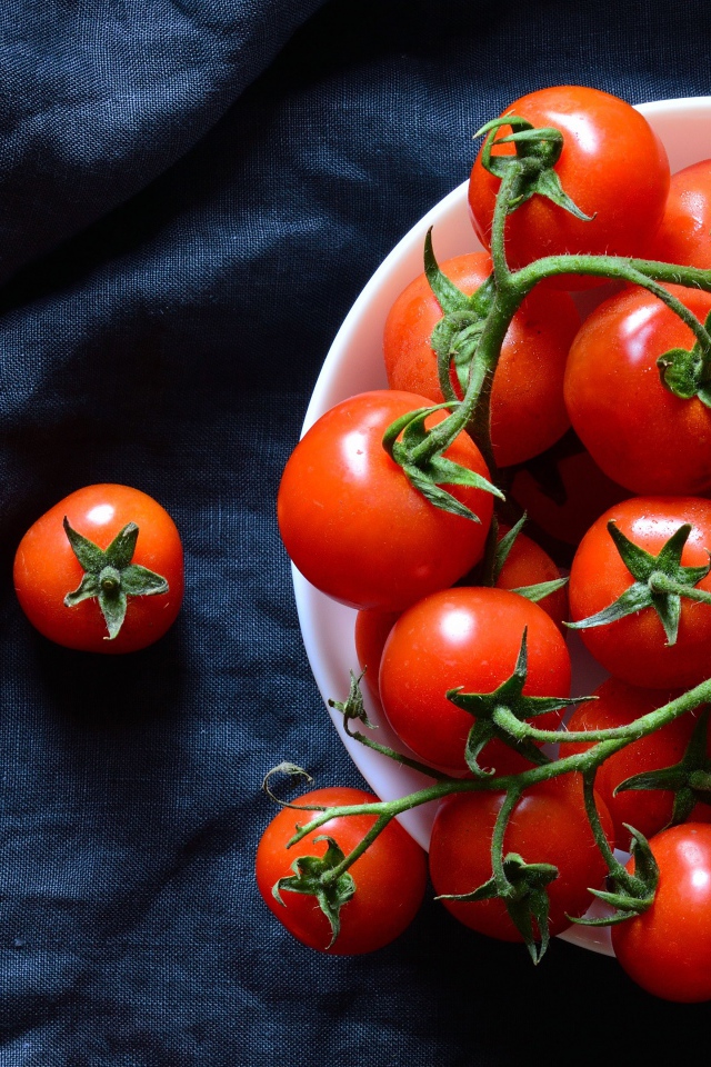 Красные помидоры в белой миске на черном фоне