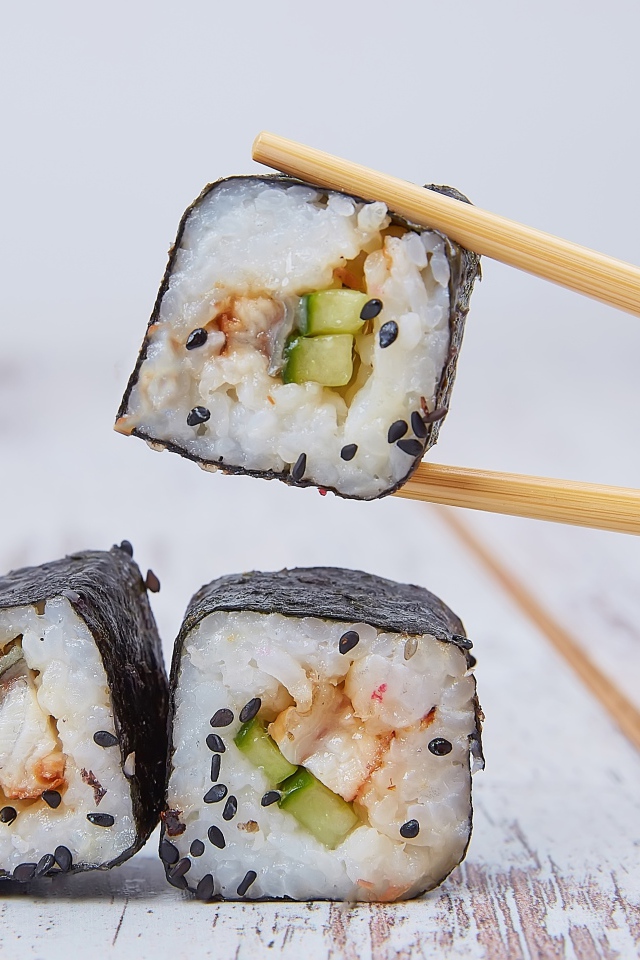 Роллы с рыбой и огурцом на столе с палочками