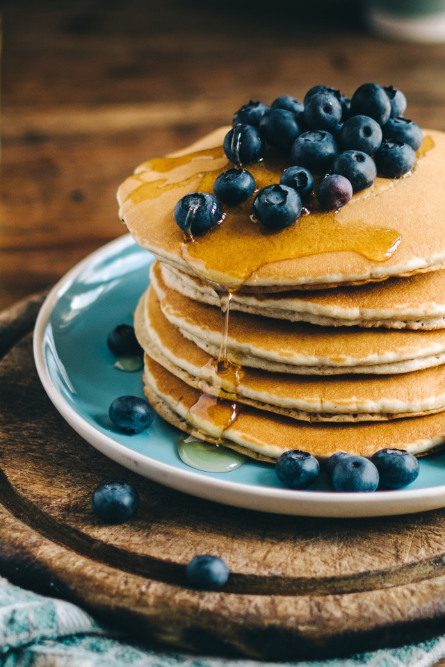 Румяные оладья на тарелке  с медом и ягодами черники 