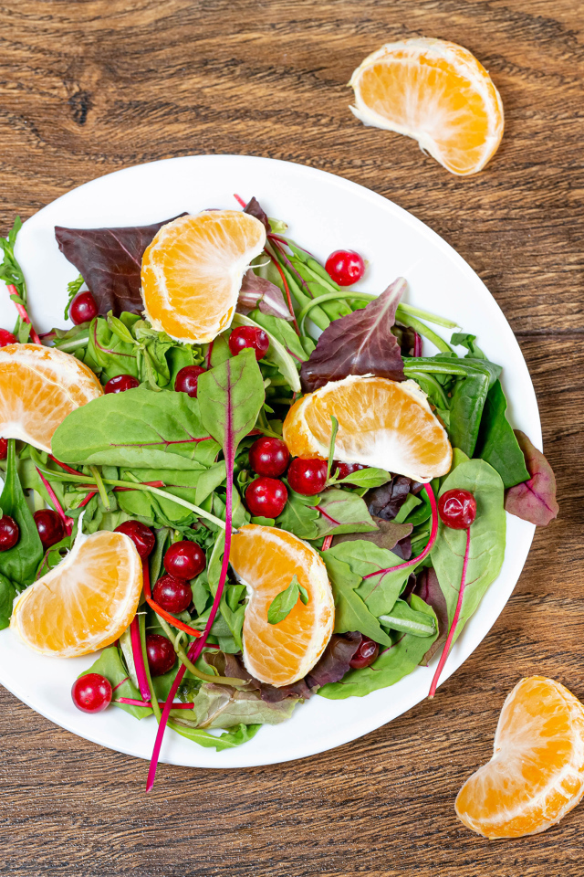 Салат из зелени и мандарина на белой тарелке на столе с вилкой