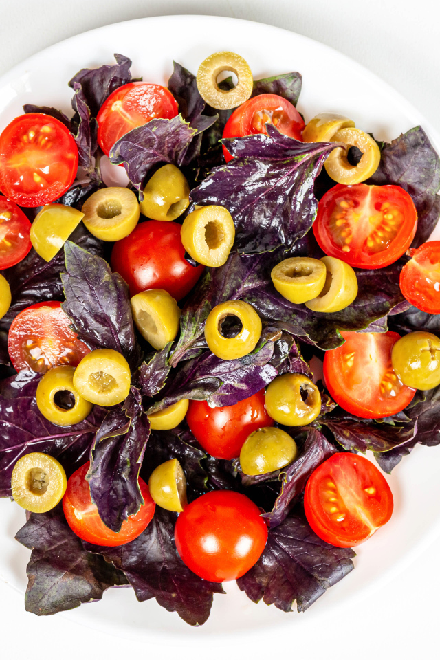 Салат с листьями базилика, помидорами и оливками на белом фоне