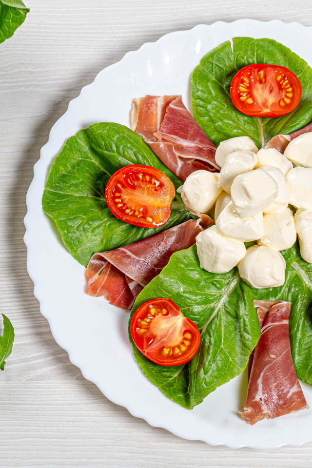 Кусочки ветчины на тарелке с сыром, помидорами и листьями салата