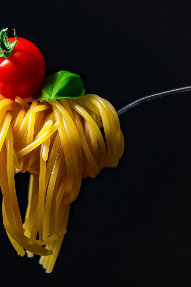 Спагетти с помидором на вилке на черном фоне