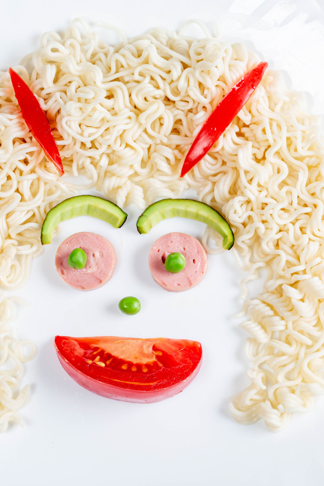 Лицо из вермишели с овощами и колбасой на белой тарелке 