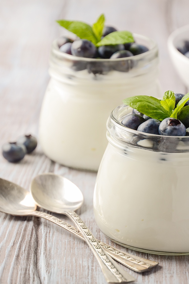 Йогурт в банках с ягодами черники на столе с ложками и медом