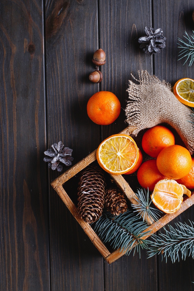 Ящик с мандаринами и шишками на столе с еловыми ветками