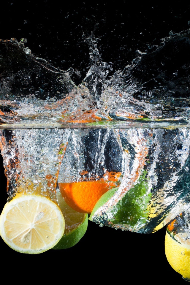 Цитрусовые фрукты падают в воду на черном фоне