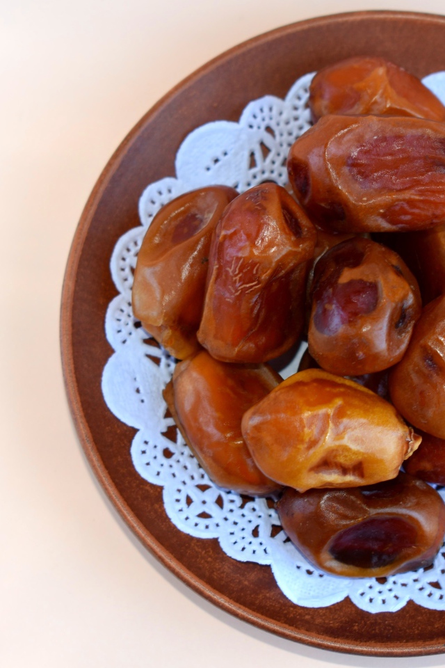 Сушеные финики в деревянной миске на белом фоне