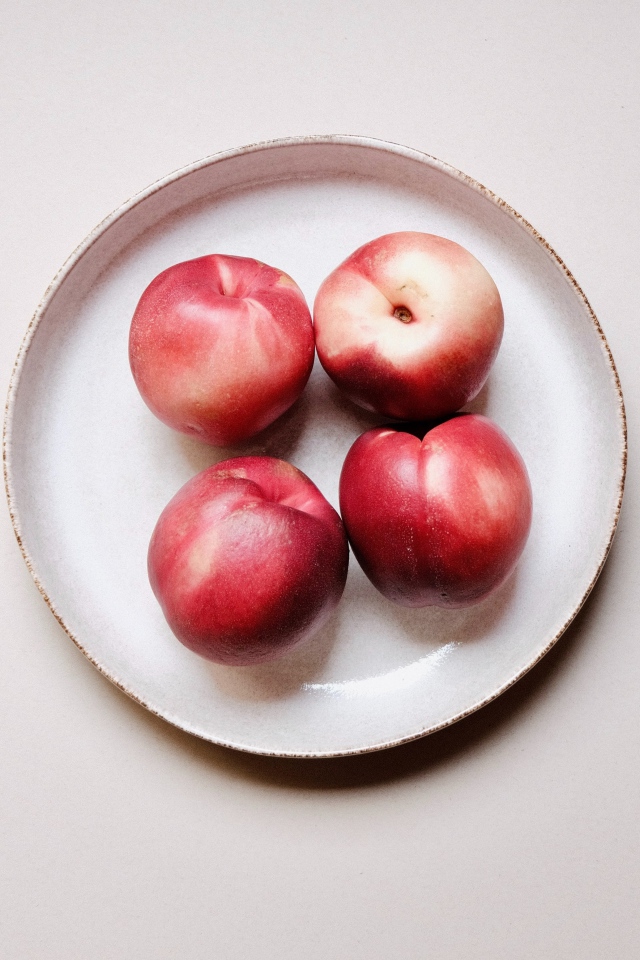 Четыре красных спелых нектарина на тарелке 