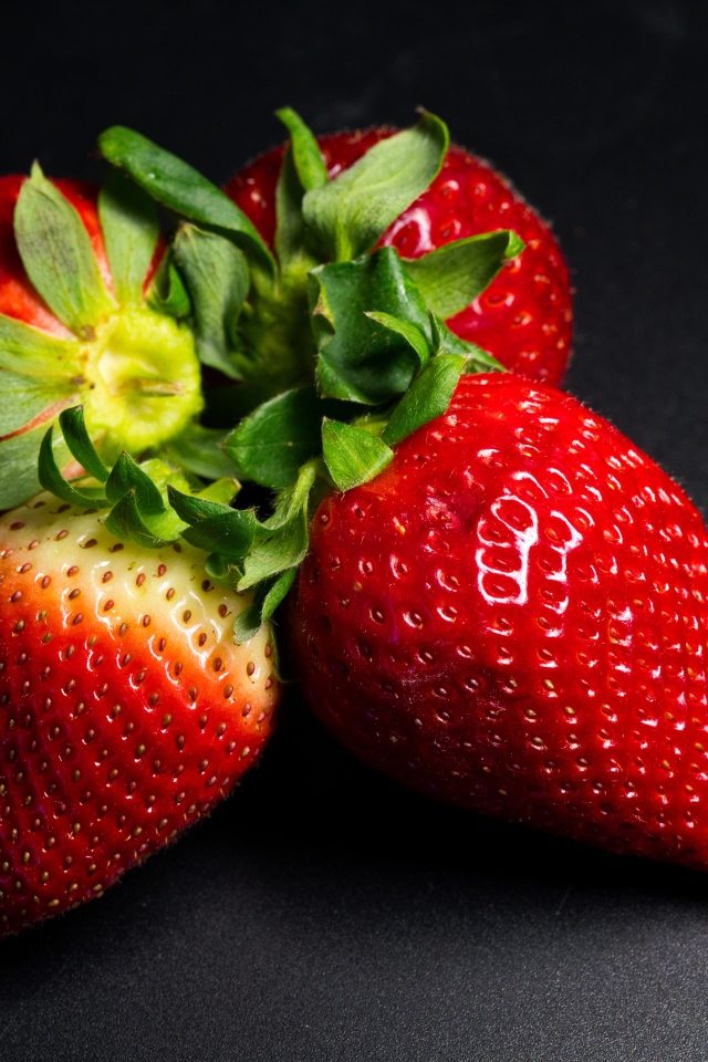 Четыре спелых красных ягоды клубники на черном столе 