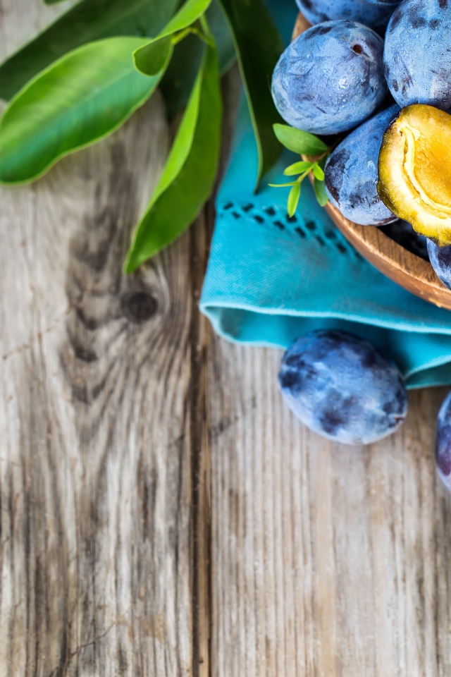 Свежие синие сливы с зелеными листьями на столе 