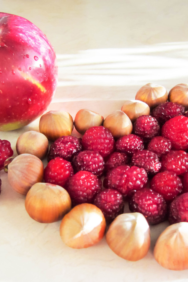 Сердце из лесных орехов и малины на столе с красным яблоком