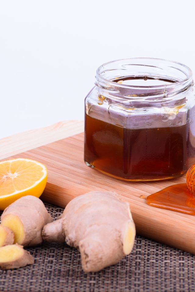 Банка меда на доске с лимоном и корнем имбиря 
