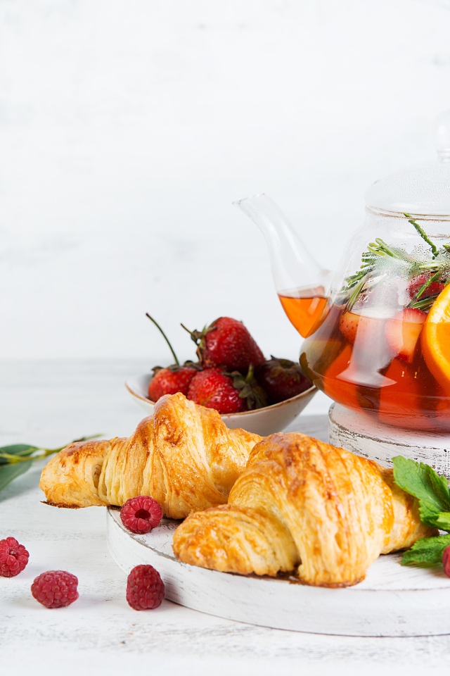 Kettle with lemon and strawberries on a table with croissants
