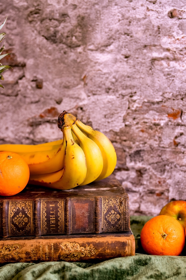 Апельсины, бананы, яблоки и ананас на столе со старыми книгами