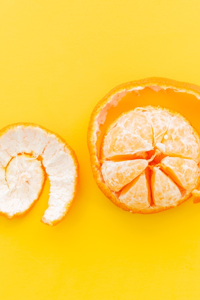 Очищенный мандарин с кожурой на желтом фоне 