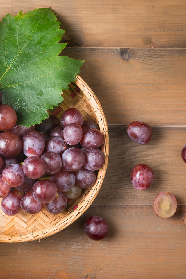 Розовый виноград с зелеными листьями на деревянном столе 