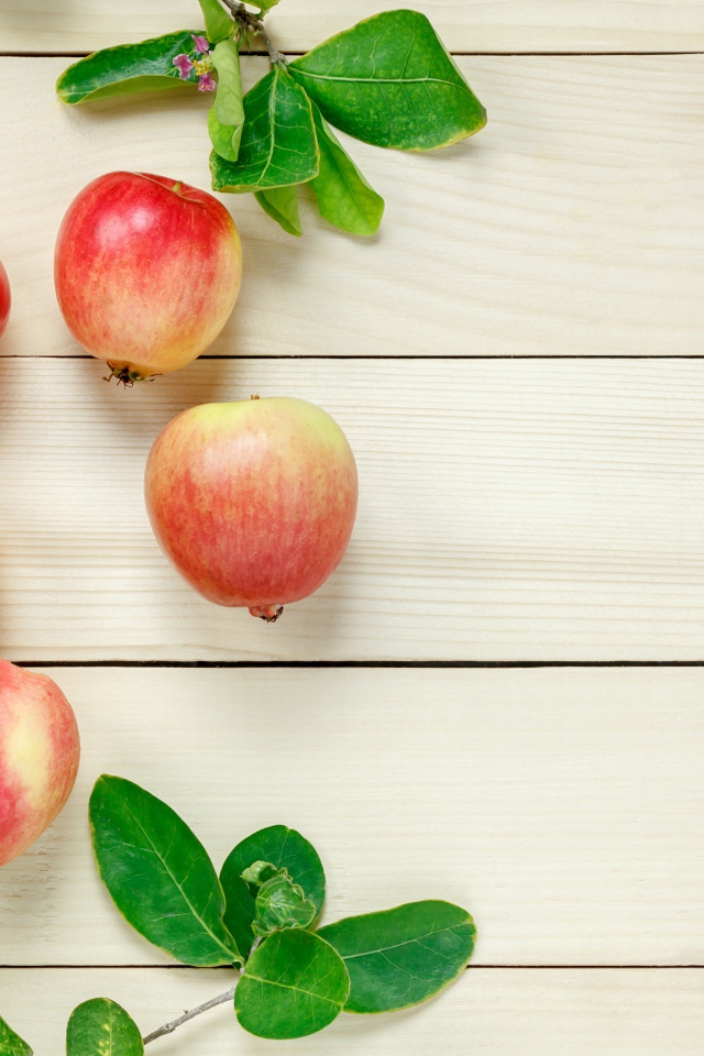 Красные яблоки с зелеными листьями на деревянном столе 