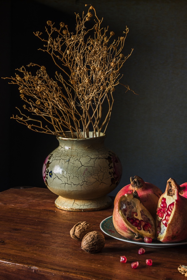 Красный гранат на столе с грецкими орехами и сухой веткой в вазе