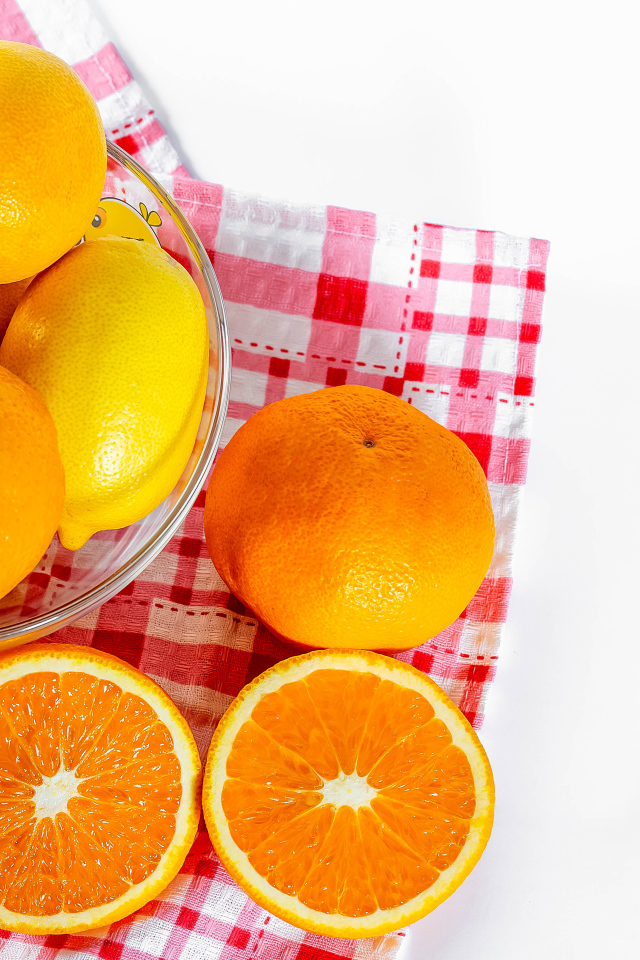 Спелые апельсины и лимоны в стеклянной миске на столе