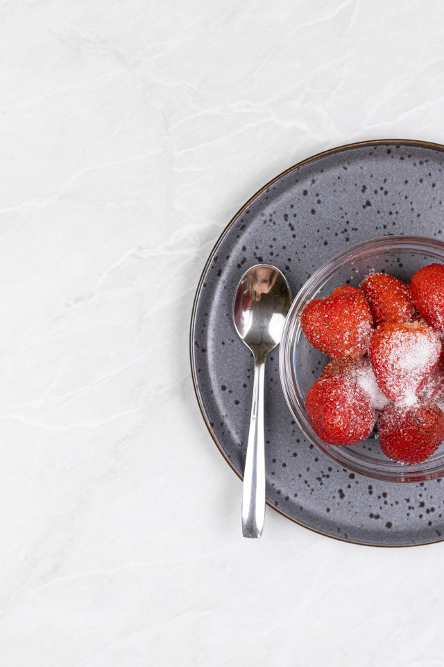 Спелая красная клубника в миске с сахаром на белом фоне