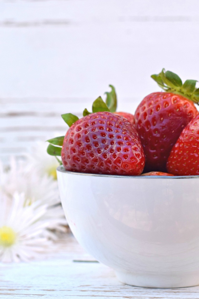 Спелая клубника в белой миске на столе с ромашками
