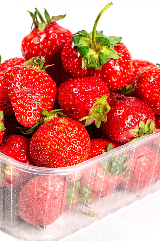 Спелая вкусная клубника в пластиковом контейнере на белом фоне