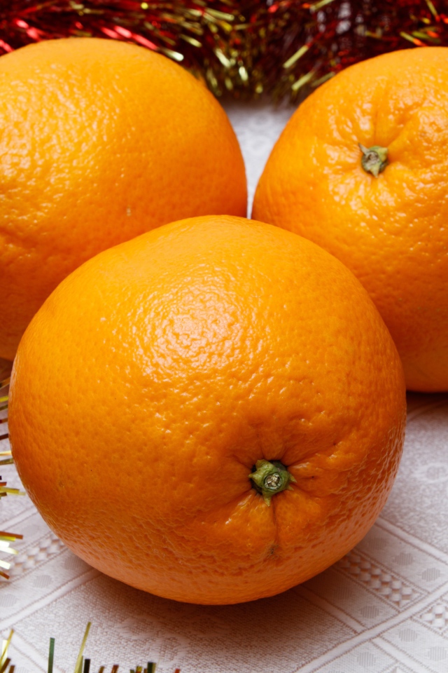 Три больших апельсина на столе с мишурой 