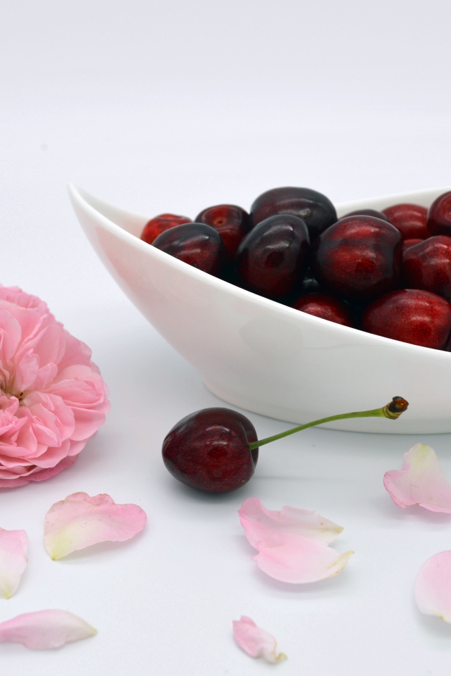 Белая тарелка с красными ягодами черешни на столе с цветами