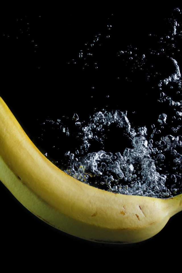 Желтый банан в воде на черном фоне