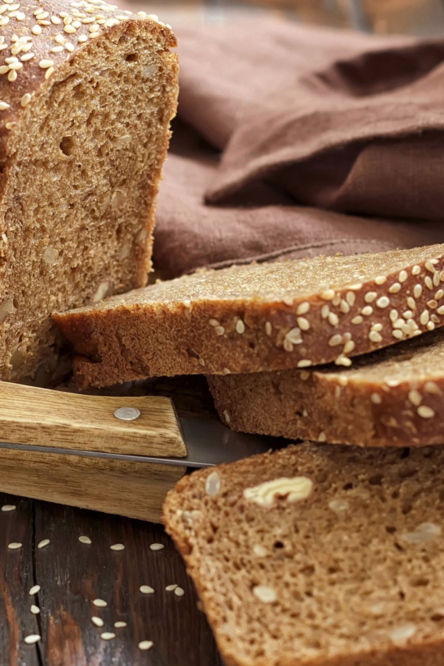 Буханка хлеба нарезанная кусочками на столе с ножом