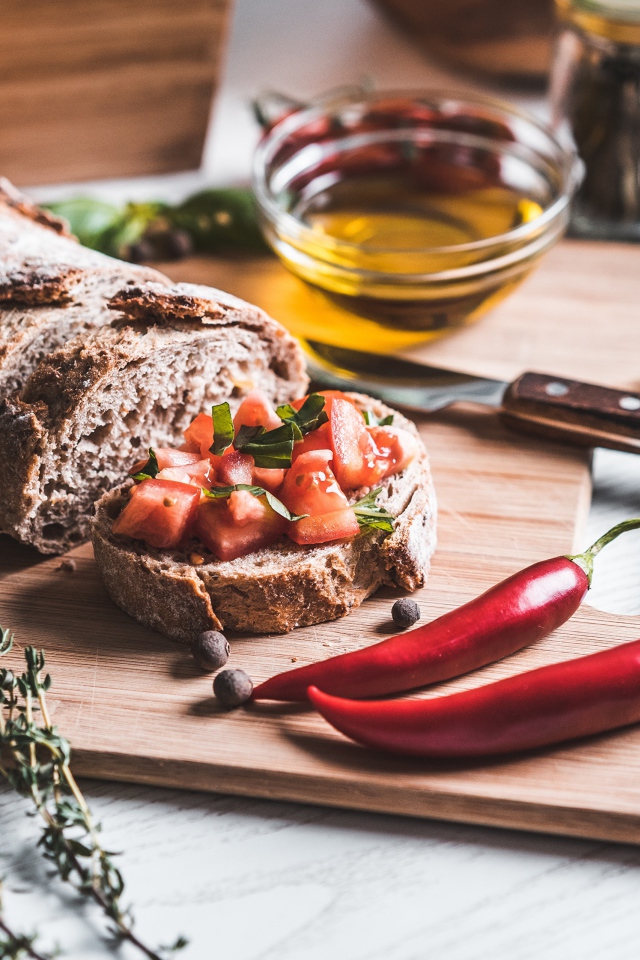 Батон с помидорами и красным перцем на столе с маслом