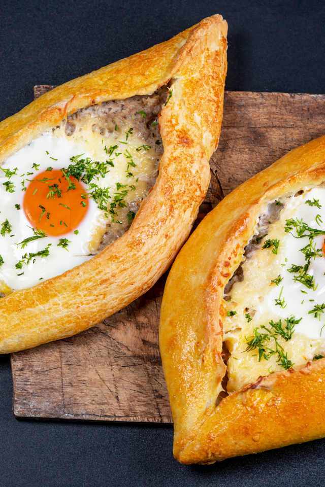 Два больших свежих хачапури с яйцом на доске