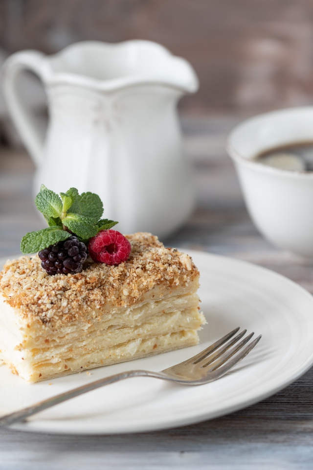 Кусок торта лежит на белой тарелке на столе с кофе