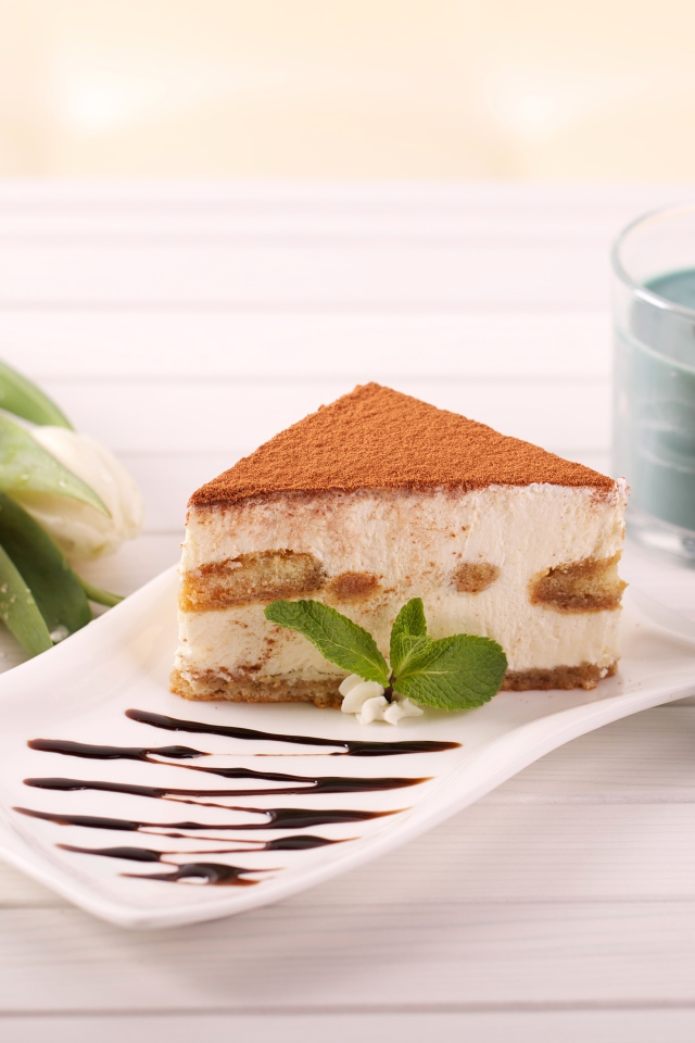 Кусок тирамису на столе с зажженными свечами и букетом тюльпанов