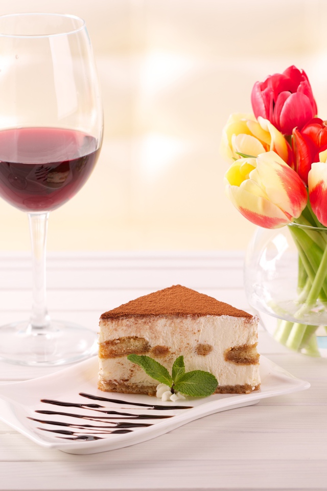 Кусок  тирамису на столе с бокалами вина и букетом тюльпанов