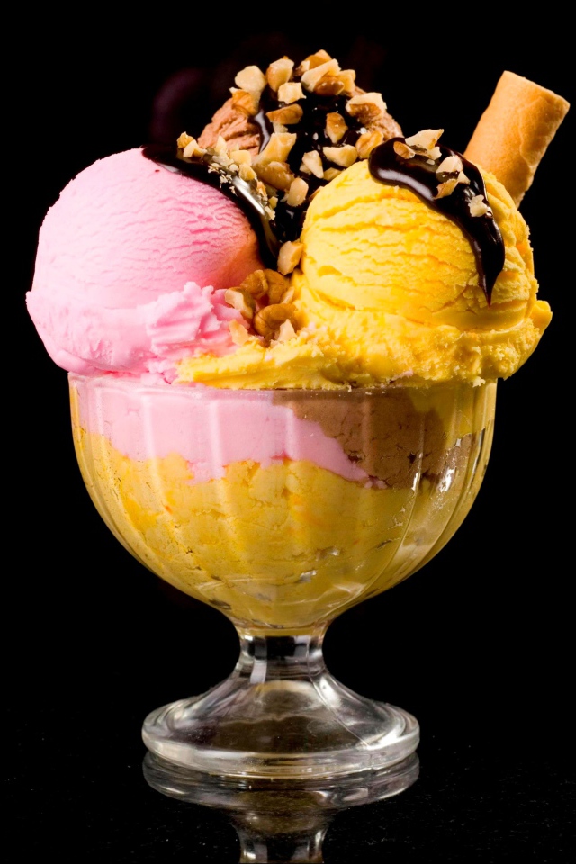 Шарики фруктового мороженого в креманке с орехами и шоколадом на черном фоне