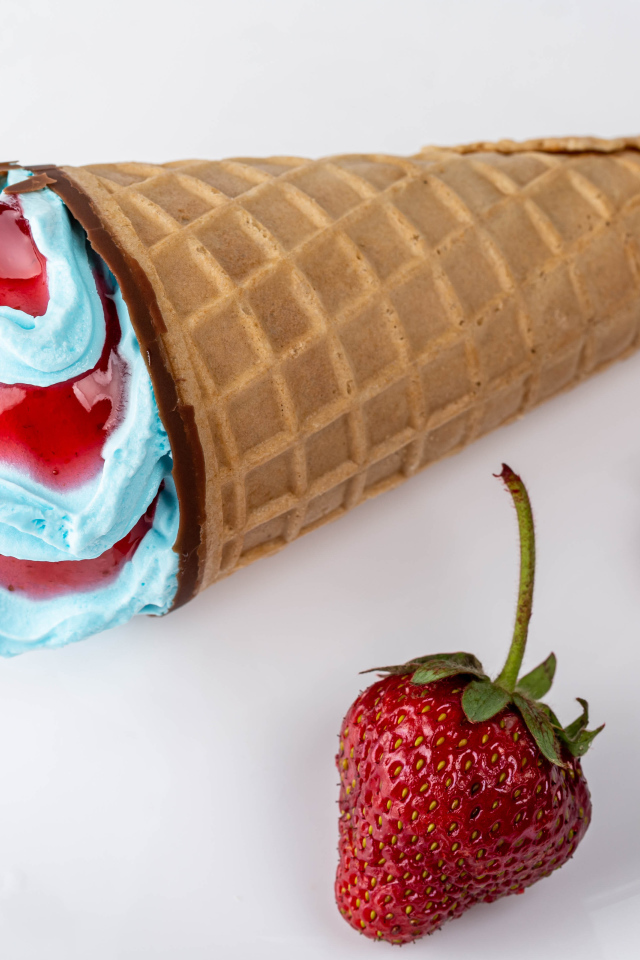 Рожок с голубым мороженым на сером фоне с клубникой 