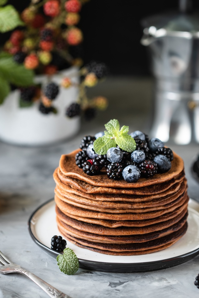 Гречневые блинчики с ягодами на столе с медом