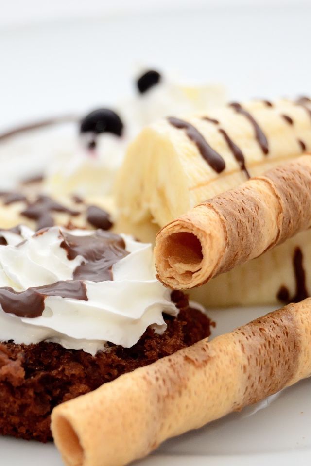 Пирожное на тарелке с бананом и сладкими трубочками