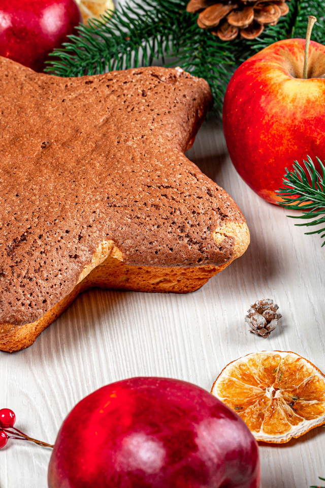 Рождественский кекс на столе с еловыми ветками,  яблоками и шишками