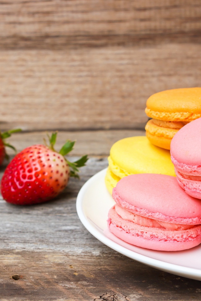 Разноцветный десерт макарун на белой тарелке на столе с клубникой