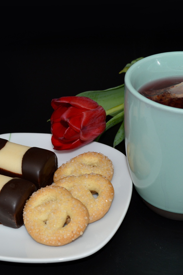 Печенье с конфетами на столе с чашкой чая и тюльпаном