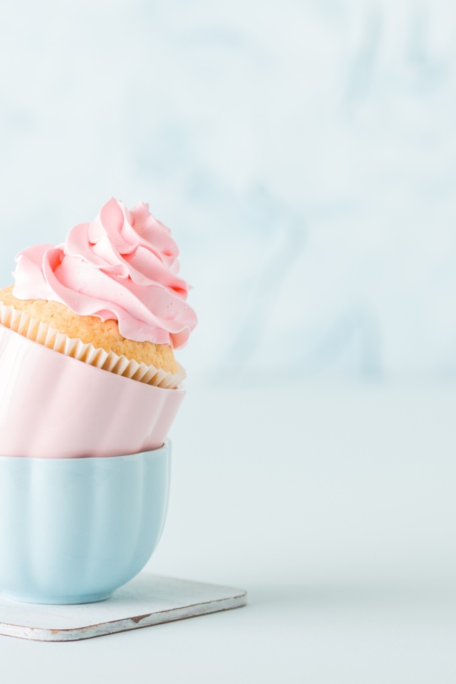 Кекс с розовым кремом с чашками на столе 