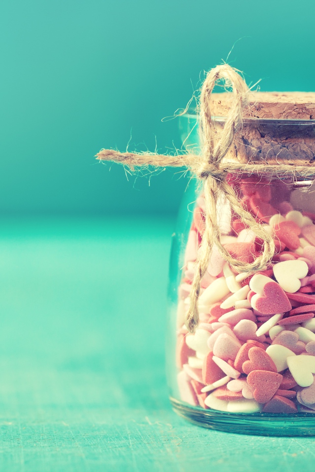 Стеклянная банка с маленькими конфетами в форме сердца на голубом фоне